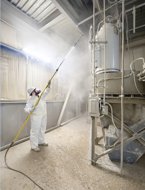 Worker performing dust mitigation with fine mist spray inside an industrial facility