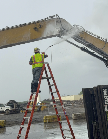Worker pressure washing heavy excavator equipment